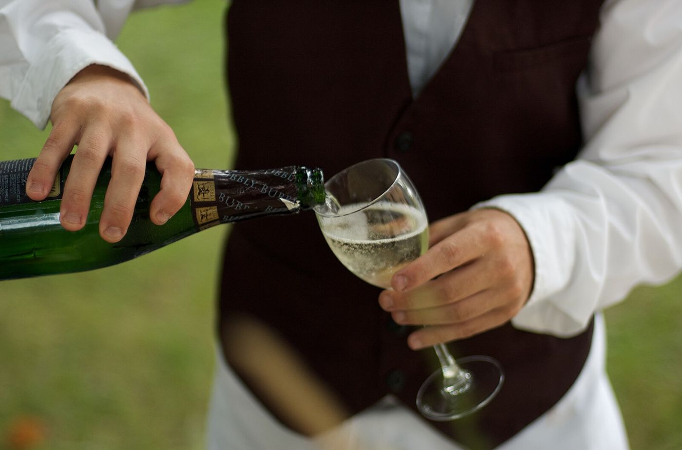 A server in a waistcoat pouring a drink at the table