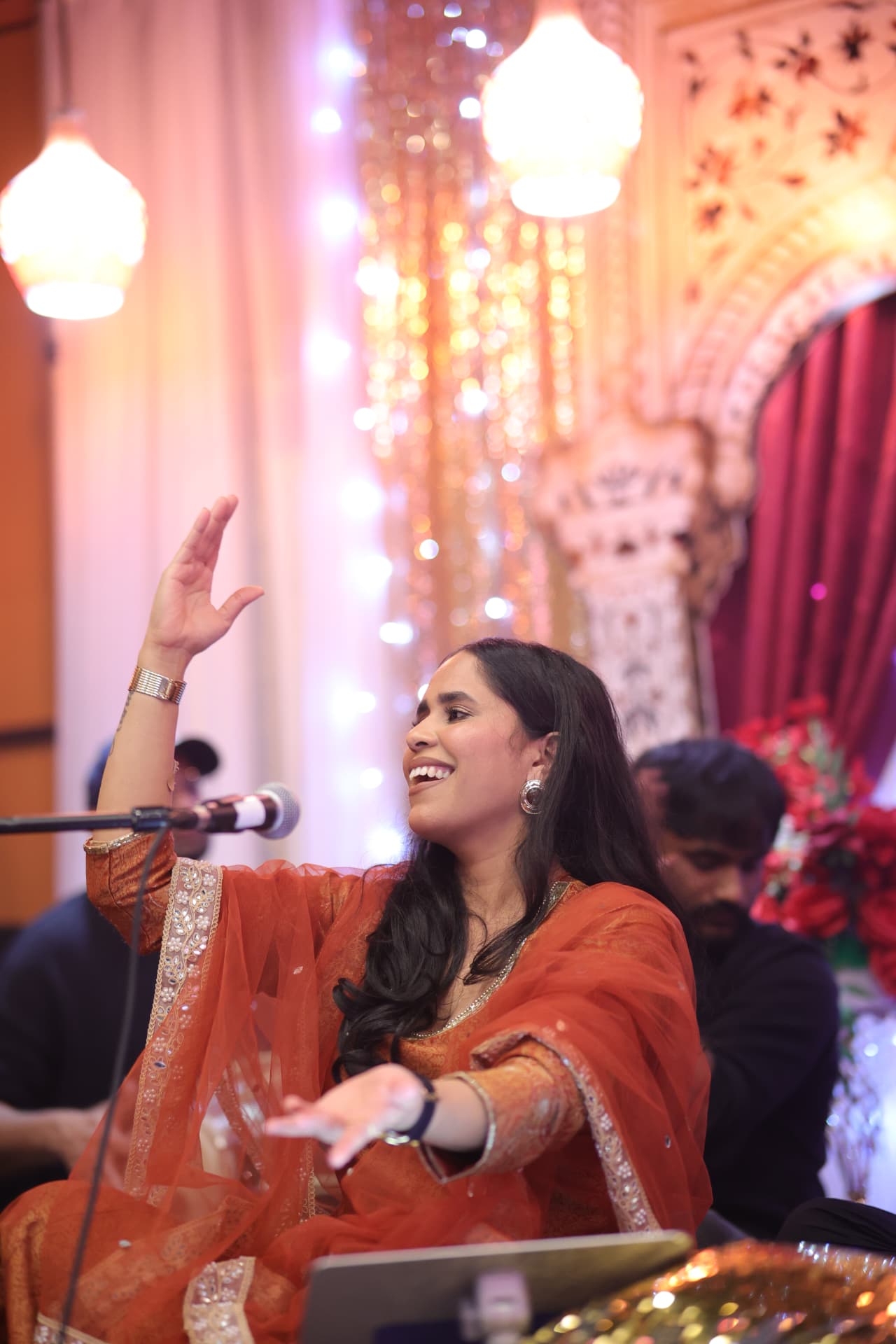 Vandna singing in an orange outfit on an ornate stage